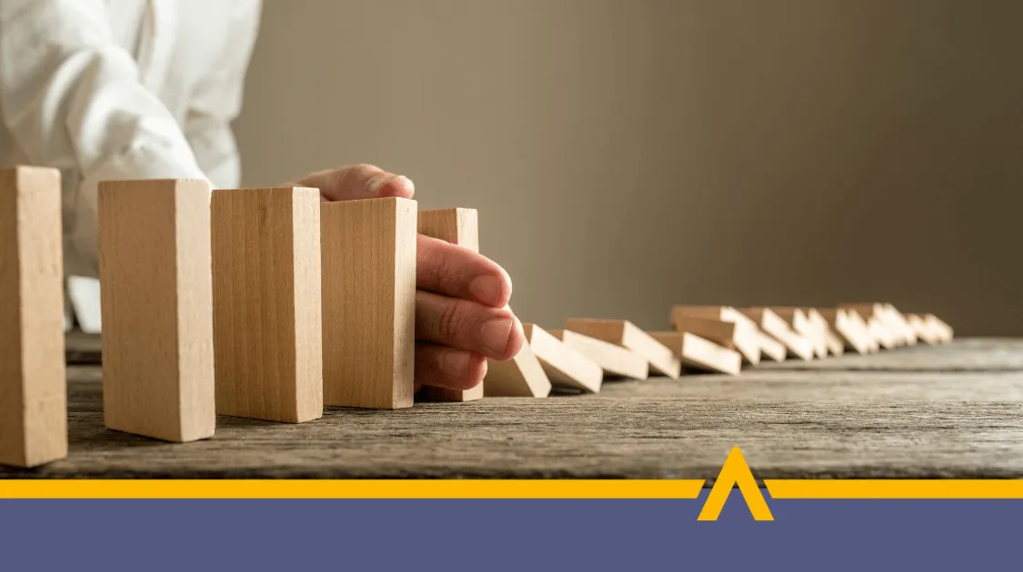 Ręka zatrzymująca przewracające się drewniane klocki na stole – symbol zatrzymania negatywnej reakcji łańcuchowej i zapobiegania konsekwencjom opóźnień w spłacie pożyczki.